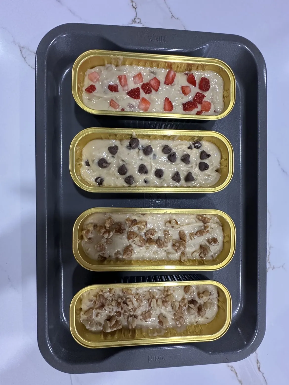 Mini banana bread batter in gold loaf trays, ready for the oven