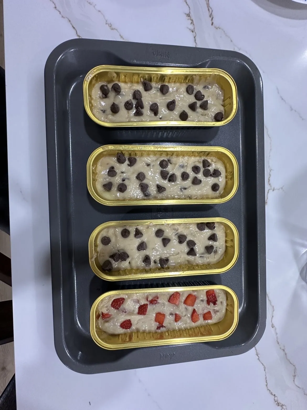 Mini banana bread batter topped with chocolate chips and strawberries, ready for the oven